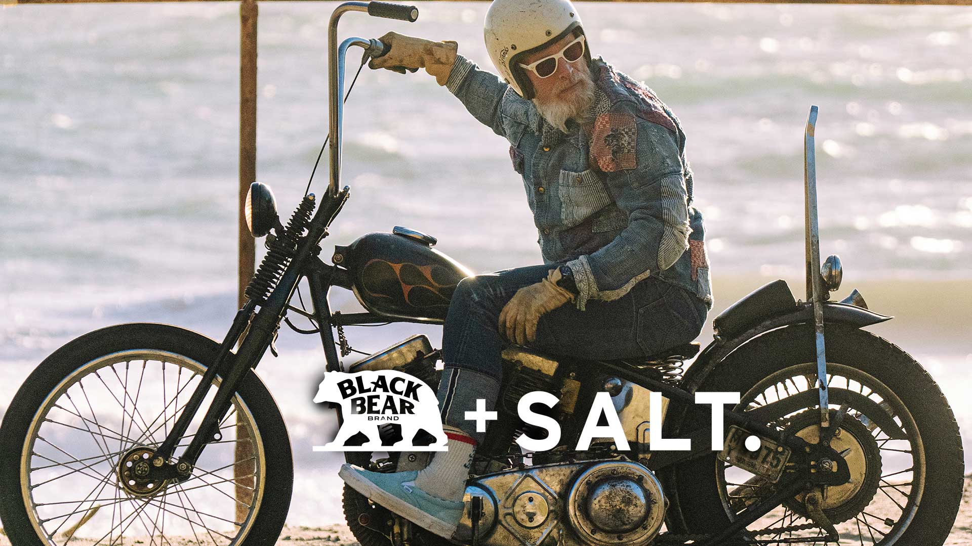 Black Bear and SALT. Collaboration header with a man on a motorcycle on the beach in sunglasses